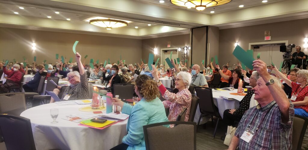 A room full of people holding up green slips of paper and smiling.