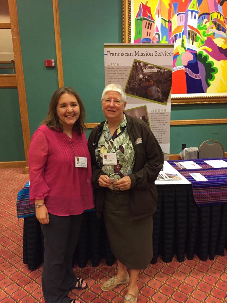 Two women with name tags stand in front of an exhibitor table.