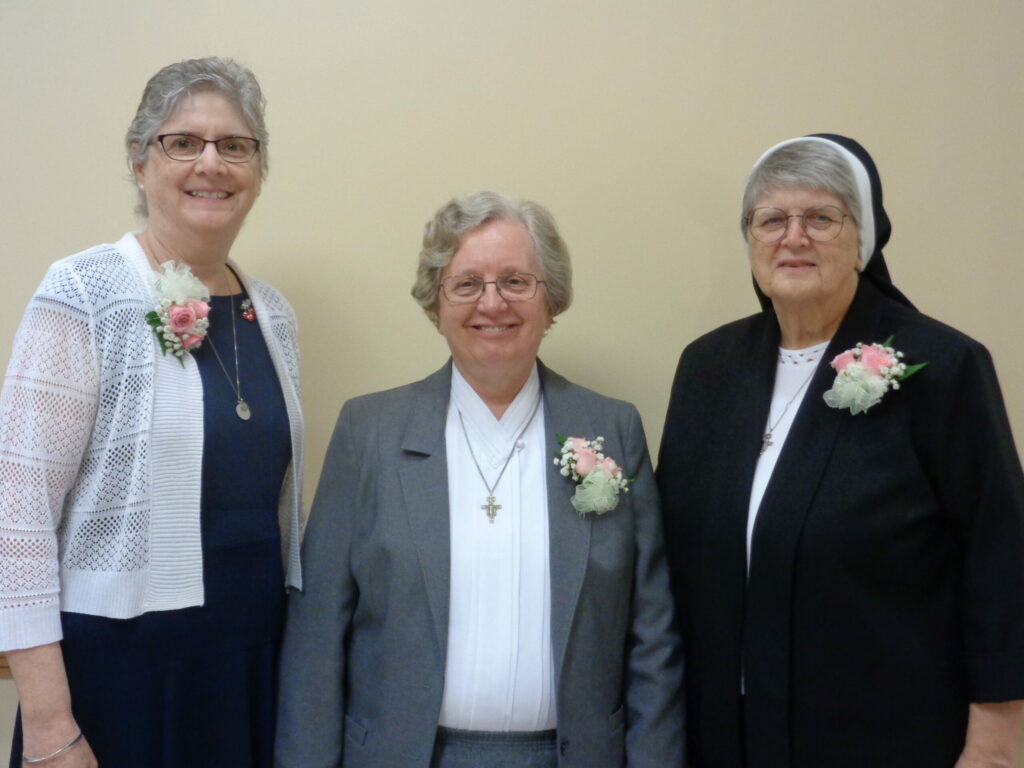 Three women standing together with rose corsages on their lapels. 