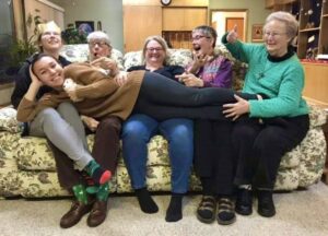 Six people of diverse ages laughing together on a couch.